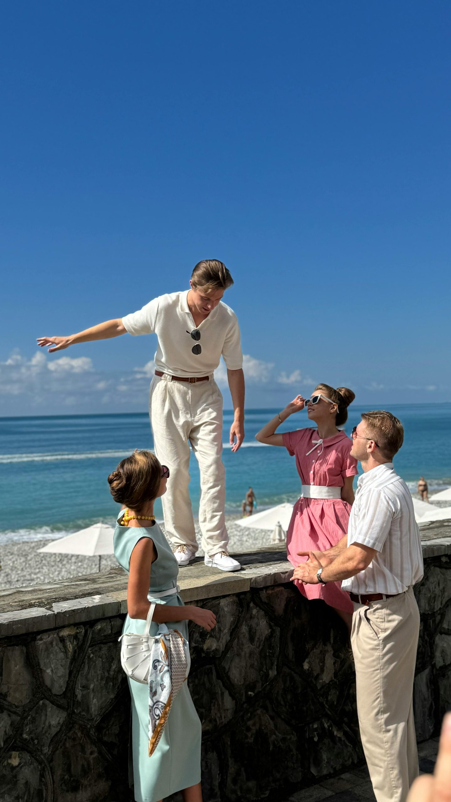 Retro-styled friends enjoy a sunny beach day with blue skies and ocean views.