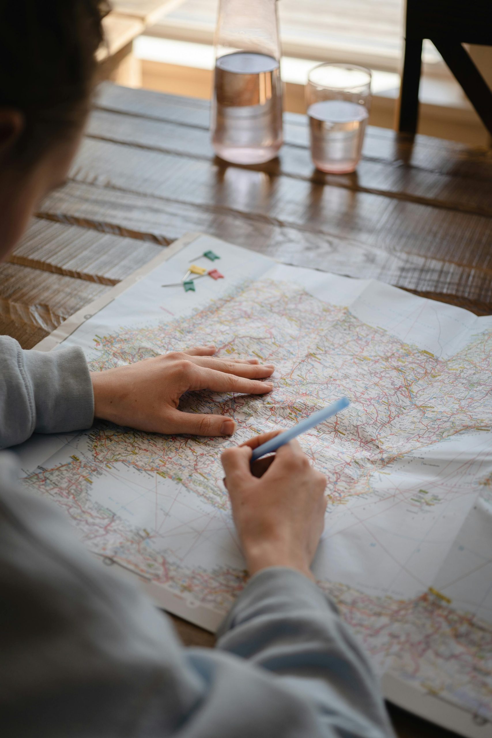 Individual marking destinations on a map with a pen while drinking water indoors.